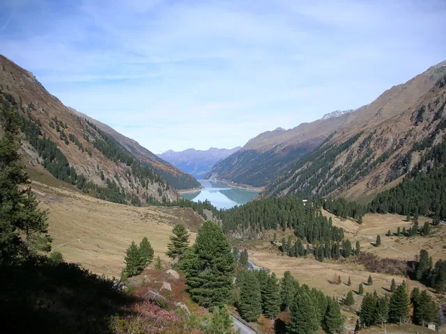 Bergtal mit See, von Nadelwäldern und felsigen Berghängen eingerahmt.