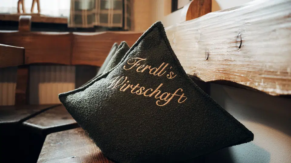 Kissen mit goldener Schrift Ferdl's Wirtschaft auf Holzbank