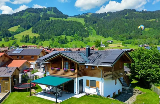 Holzhaus mit Solarpanelen vor grünem Alpenidyll