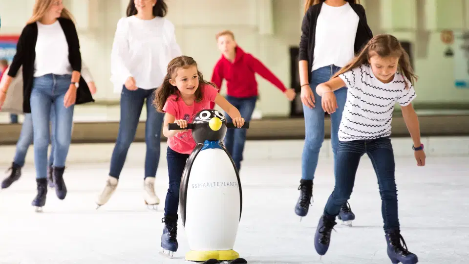 Kind mit Pinguin-Laufhilfe beim Eislaufen