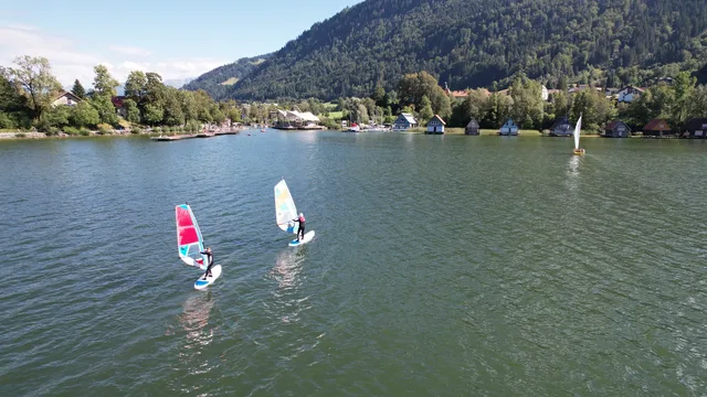 Windsurfer auf einem ruhigen See, umgeben von Häusern und Bergen
