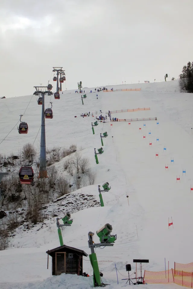 Sesselbahn fährt über verschneite Piste mit Pistenmarkierung und Skifahrern.