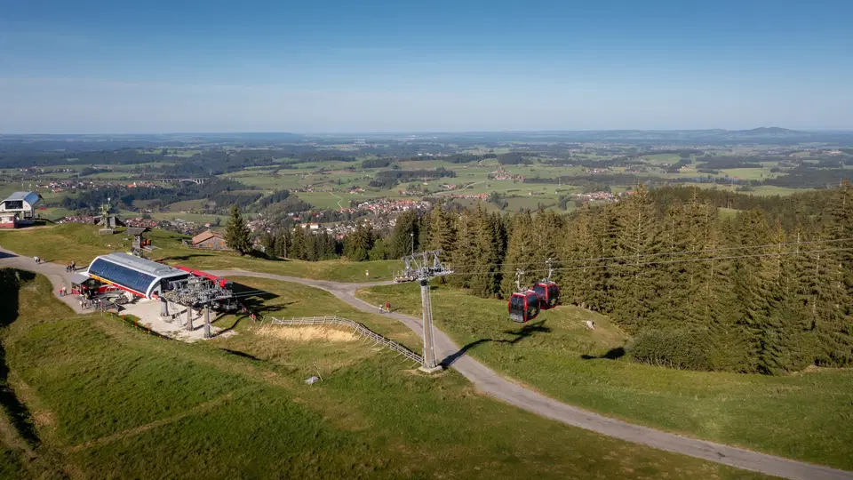Berglandschaft mit Seilbahn, Lifttrasse und roter Kabine auf grünem Hügel.