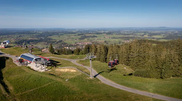 Berglandschaft mit Seilbahn, Lifttrasse und roter Kabine auf grünem Hügel.