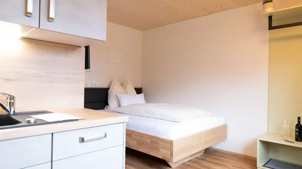 Studioapartment mit Bett, Kochnische und Holzboden.