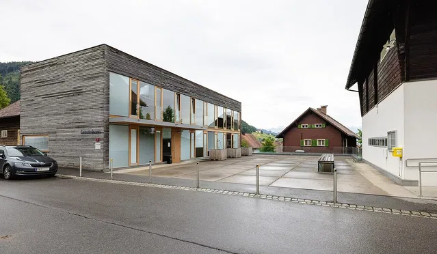 Modernes Holzgebäude mit Glasfronten am Straßenrand und Parkfläche im Hintergrund.