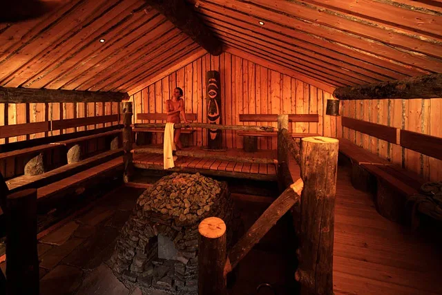 Saunaraum aus Holz mit Steinofen und einer Person am Ofen.