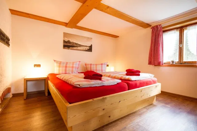 Gemütliches Schlafzimmer mit Holzbalken, Doppelbett in roter Bettwäsche und zwei roten Handtüchern