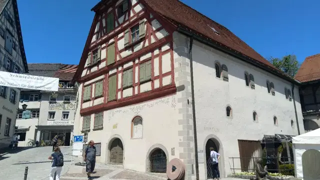 Fachwerkgiebel der Eselmühle in Wangen mit Brunnen und Menschen auf dem Vorplatz sowie einem Wasserrad an der Gebäudeseite. Ortsmotiv.