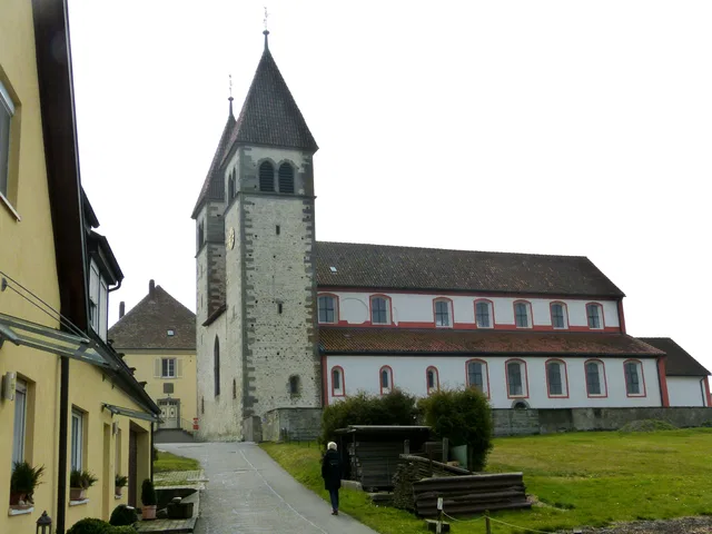 Kirchturm und Kirchengebäude mit Nebenhäusern und Weg davor