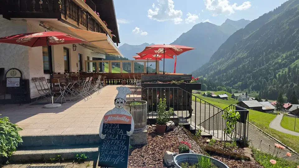 Terrasse des Starzelhauses mit roten Sonnenschirmen vor Berglandschaft.