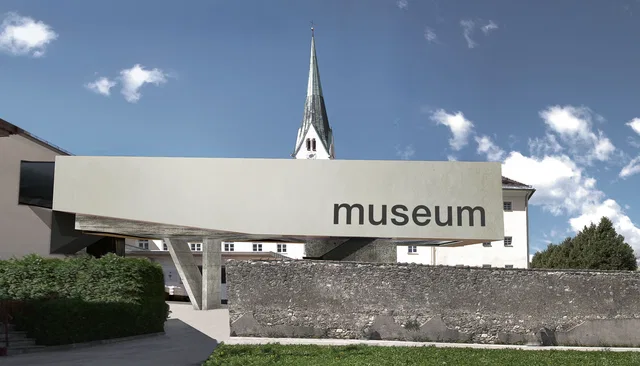 Moderner Museumsbau vor einer Kirche mit spitzem Turm