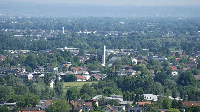 Luftaufnahme einer grün geprägten Stadtlandschaft mit Turm im Zentrum.