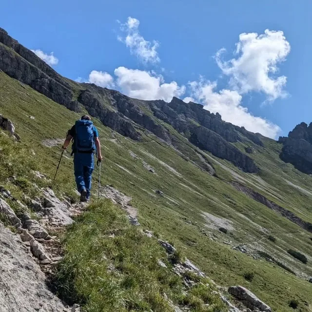 Wanderer mit blauem Rucksack und Trekkingstöcken auf steilem Bergpfad