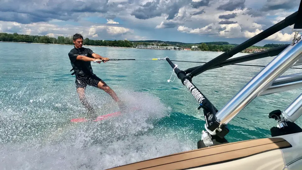 Wakeboarder wird von einem Boot über glitzerndes Wasser gezogen, Wasser spritzt.