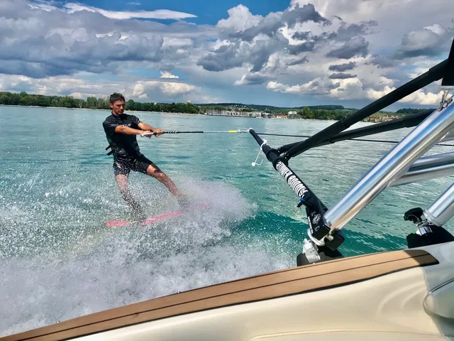 Wakeboarder wird von einem Boot über glitzerndes Wasser gezogen, Wasser spritzt.