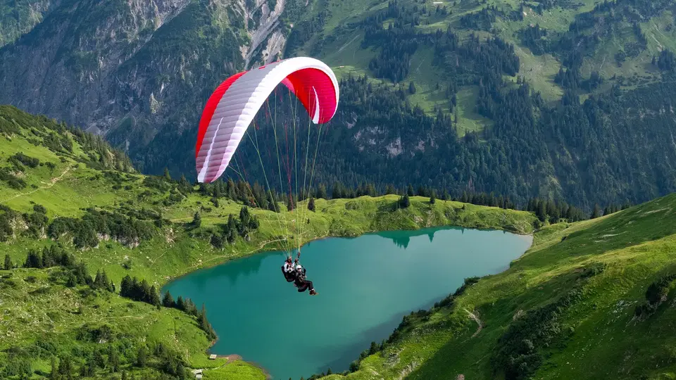 Paraglider über alpinem Bergsee vor Bergkulisse.