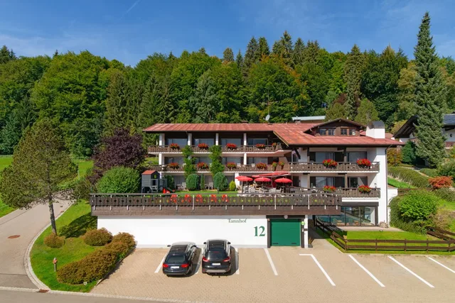Hotelgebäude mit Balkonen, roten Blumen, Parkplätzen und umliegender grüner Natur.