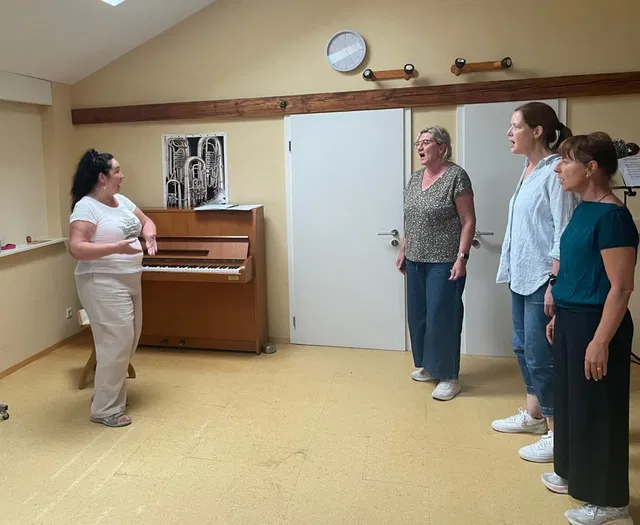 Frau erklärt am Klavier eine Gruppe von drei singenden Frauen.