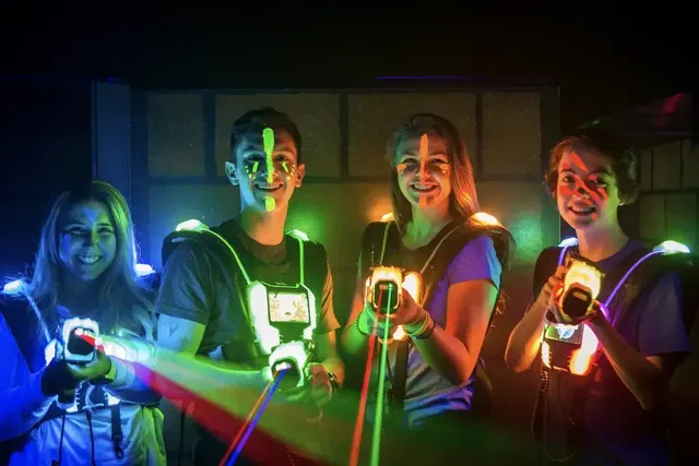 Vier Personen mit leuchtenden Westen und Lasergeräten in der Lasertag-Arena.
