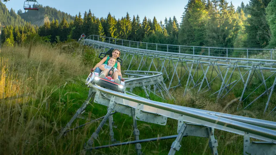 Zwei Gäste fahren mit dem AlpspitzCOASTER durch Wald und Wiesen