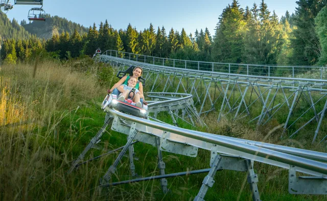 Zwei Gäste fahren mit dem AlpspitzCOASTER durch Wald und Wiesen