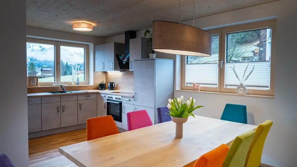 Küche und Essbereich des Wohlfühlapartments mit Holztisch und bunten Stühlen.