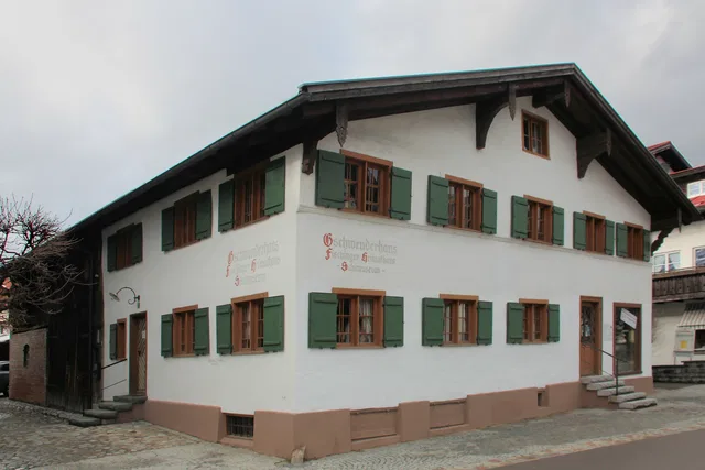 Traditionelles weißes Haus mit grünen Fensterläden und Holzdachüberstand.