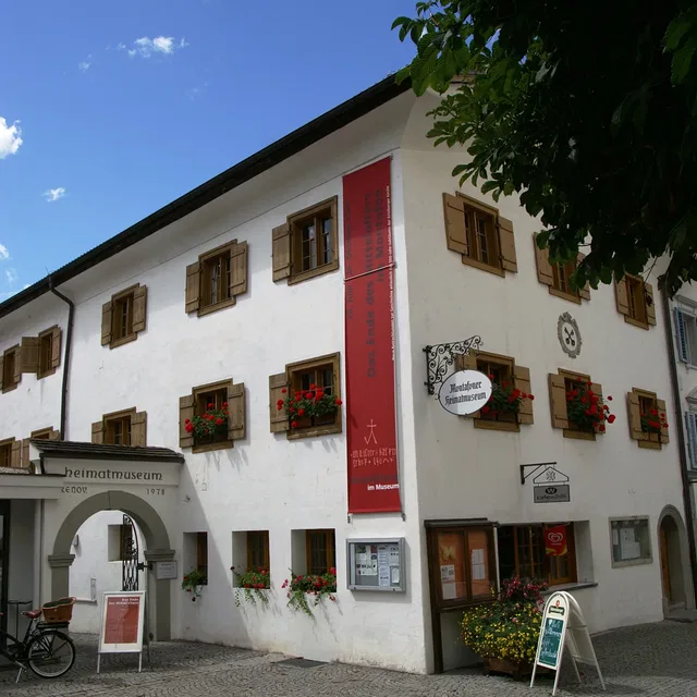 Weißes Museumsgebude mit Holzkfenstern, Blumenksten und roten Bannern an der Fassade