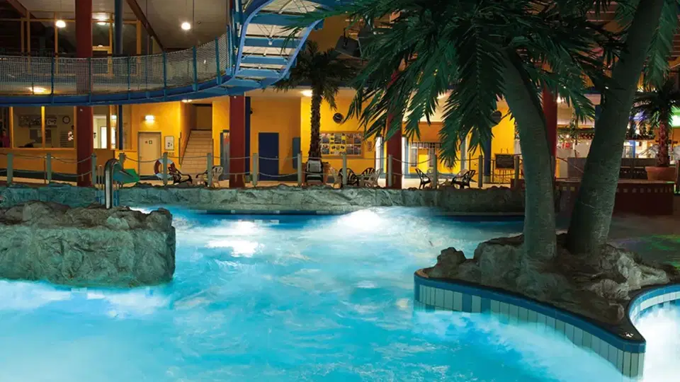 Indoor-Schwimmbad mit Palmen, Felsvorsprungen und blau beleuchtetem Wasser