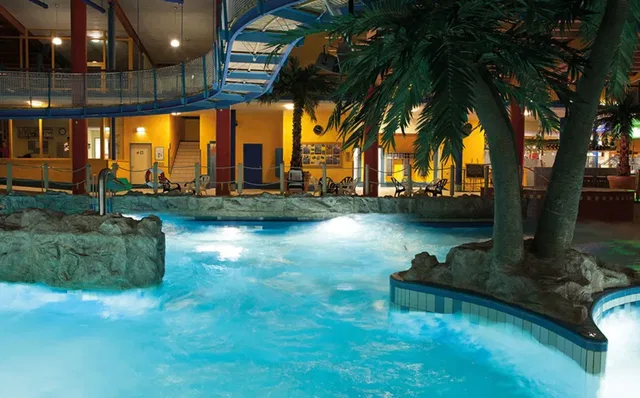 Indoor-Schwimmbad mit Palmen, Felsvorsprungen und blau beleuchtetem Wasser