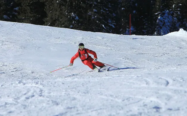 Skifahrer in rotem Anzug fährt eine enge Kurve auf einer verschneiten Piste, mit Helm und Skistöcken