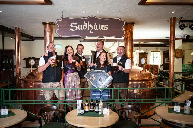 Gruppe von sechs Personen in Lederhosen und Trachten vor Sudhaus in einer Brauerei, mit Biergläsern