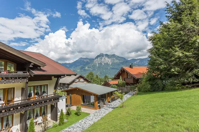 Alpine Häusergruppe mit Garten, Kiesweg und Bergblick unter blauem Himmel.