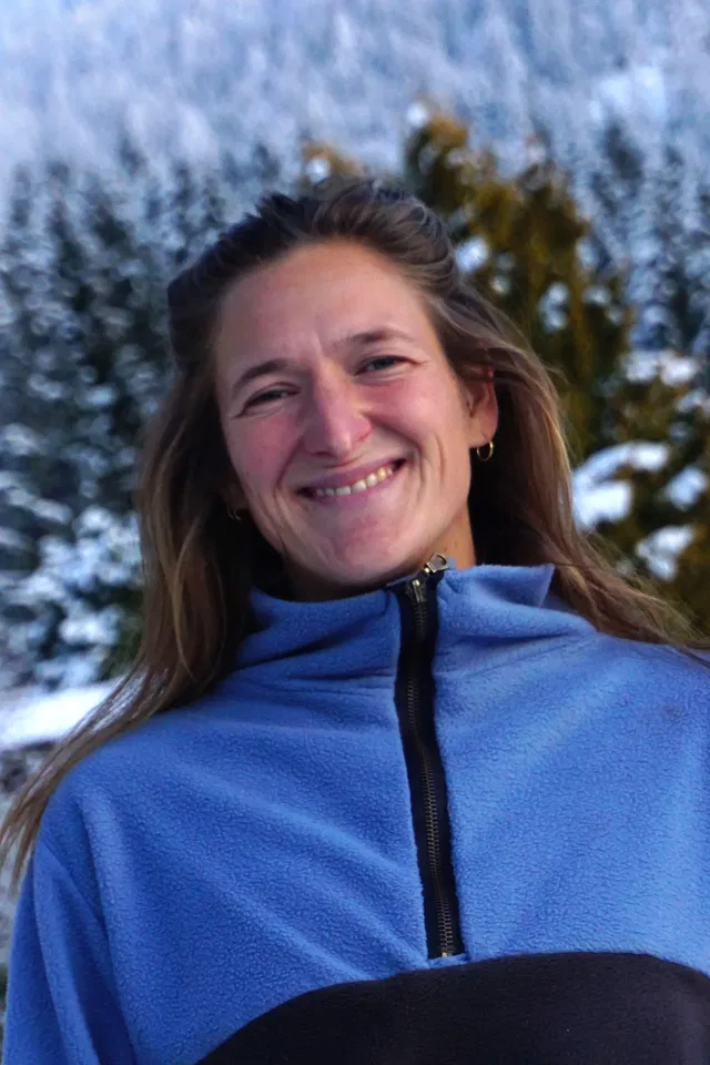 Lächelnde Frau im blauen Fleece vor verschneiten Bäumen