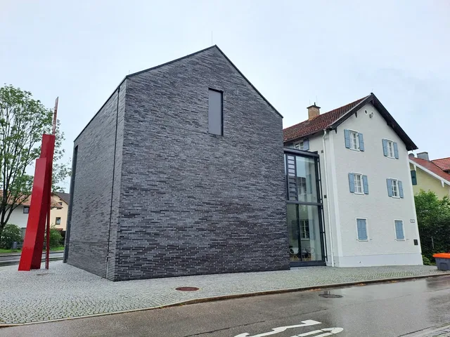 Modernes dunkles Ziegelgebäude neben einem weißen Haus