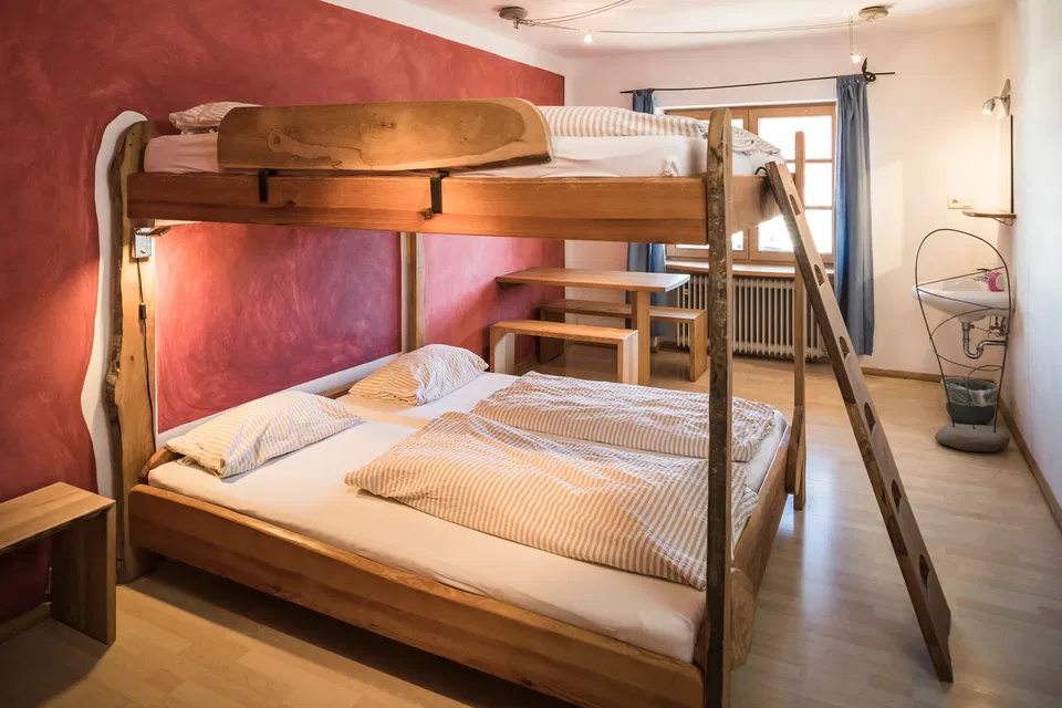 Zimmer Bazar mit breitem Holzstockbett und Leiter vor roter Wand