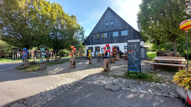 Historische Glashütte Schmidsfelden mit Holzfassade und farbigen Glaskugeln auf dem Vorplatz.