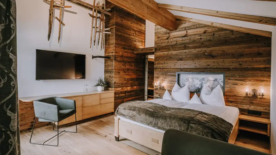 Doppelbett, Fernseher und sichtbare Holzbalken in der Suite Gaisberg.