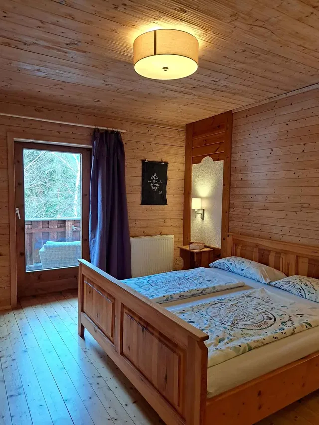 Schlafzimmer eines Holzhäuser-Appartements mit Doppelbett, Holzmöbeln und Balkonblick