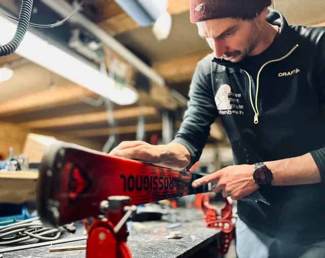 Mann bearbeitet Snowboard in Werkstatt, Kante im Fokus