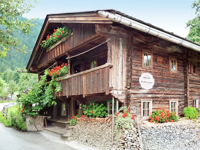 Traditionelles Holzbauernhaus mit roten Geranien vor einem bewaldeten Berghang