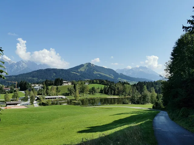Landschaft mit Wiesen, Teich, Wald und Bergen im Hintergrund