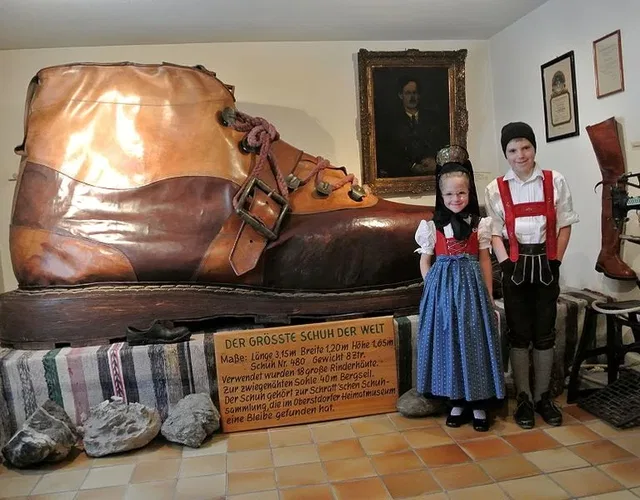 Überdimensionierter Leder-Schuh im Museum neben zwei Kindern in Trachten