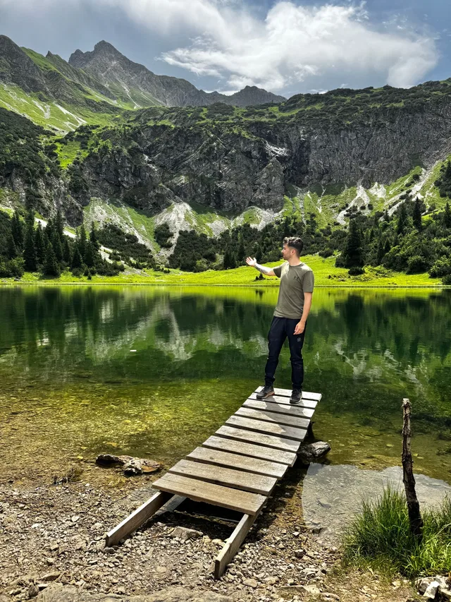 Mann auf einem Holzdock am Bergsee vor felsigen Bergen