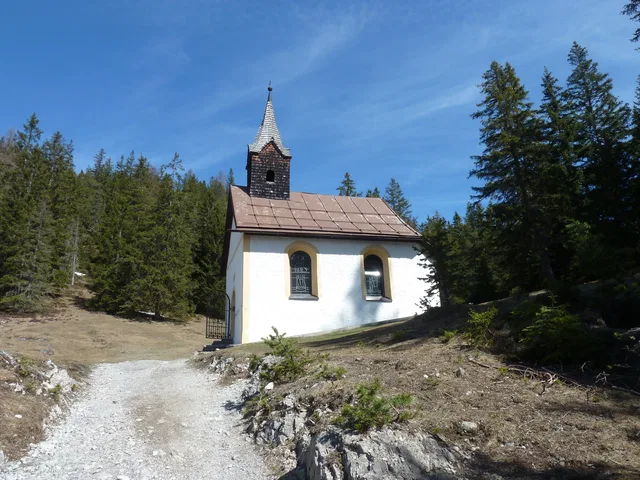 Kleine weiße Kapelle mit rotem Dach und Turm im Wald auf einem Hügel