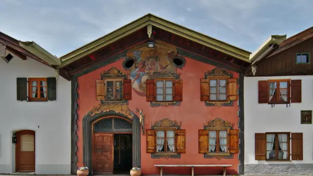 Rote Fassade des Geigenbaumuseums Mittenwald mit aufwendiger Lüftlmalerei und hölzernen Fensterläden Ortsmotiv.