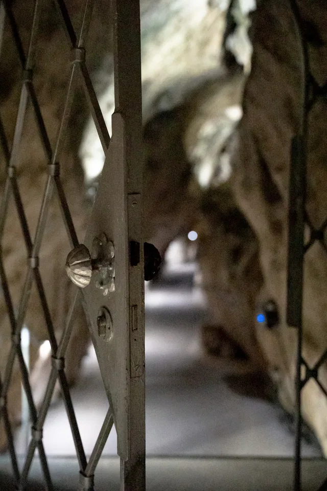 Metallgittertür in einer Höhlenpassage, Blick durch den Gang in die Tiefe.