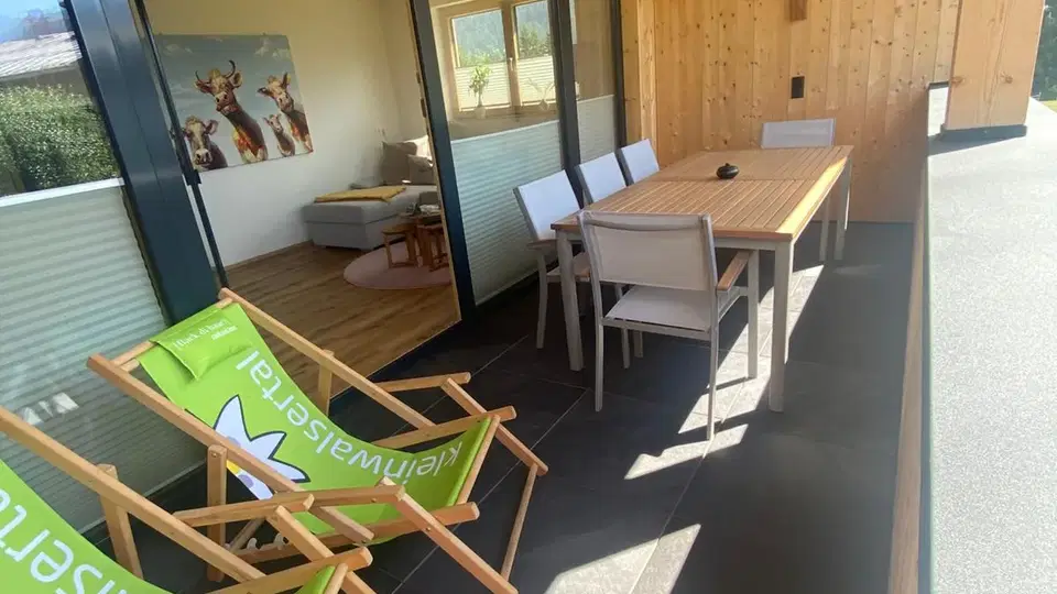Überdachter Balkon mit Esstisch und zwei grünen Liegestühlen.