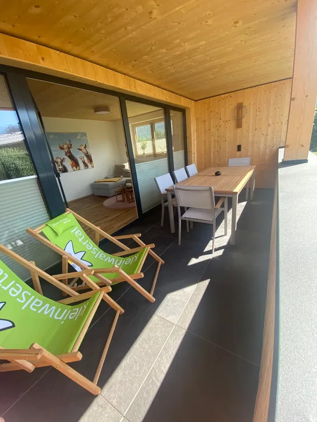 Überdachter Balkon mit Esstisch und zwei grünen Liegestühlen.